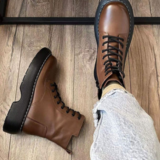 On voit une paire de bottes marron en cuir. La botte droite est au pied de quelqu'un et la botte gauche posée au sol.