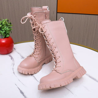 Très jolies bottes hautes, lacées, style doc martins. Elles sont toutes roses y compris la semelle en caoutchouc. Elles sont posées sur une table en marbre près d'une plante.