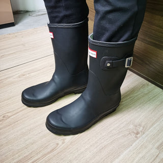 femmes en pantalon noir qui prote une paire de bottes pour jardin sur un sol en bois