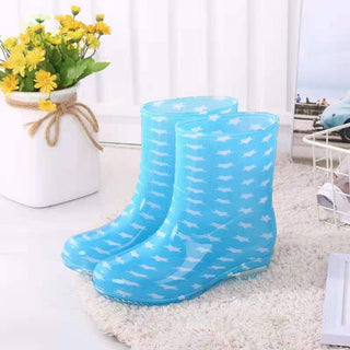 Bottes de pluie bleues claires avec des motifs d'étoiles blanches, posées sur un tapis blanc, près d'un vase avec des fleurs