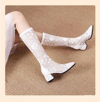 bottes blanches mi haute en dentelle avec motif de fleur à talon bas et carré, porté par une jeune femme dont on ne voit que les jambes qui sont croisées