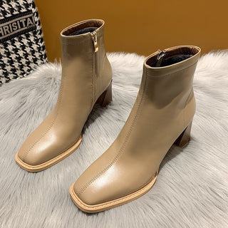 Paire de bottines beige à bout carré pour femme. Posé de trois-quart sur un tapis de fourrure gris, avec un mur marron en fond.