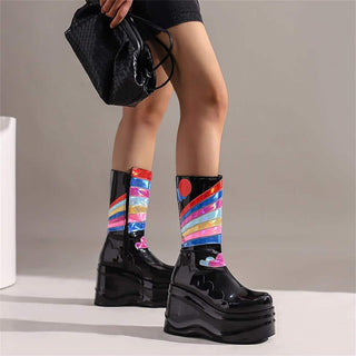 Jambes de femme portant des chaussures vernis noires à plateformes avec des couleurs au niveau des chevilles. La femme porte un sac noir et une jupe noire