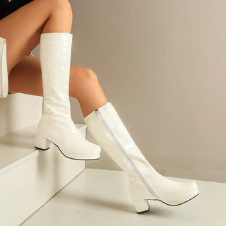 Bottes blanches en cuir vernis avec une fermeture éclair blanche portées sur un escalier blanc