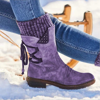 Bottes violettes avec des lacets à l'arrière portées par une femme en jean assise dans la neige avec une luge en bois derrière