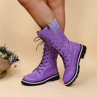 Bottes violettes à lacets portées par une femme debout les jambes croisées avec un bouquet de fleur sur le côté