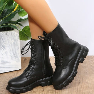 Photo de bottes militaire noires styles rangers pour femmes portées. Les demis james de la femme sont sur un parquet en bois avec une plante derrière