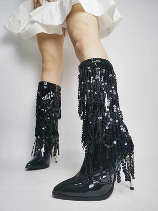 jeune femme qui porte une jupe blanche courte et dont on ne voit que les jambes, porte une paire de botte vintage noires, à talons aiguilles, avec des franges en strass