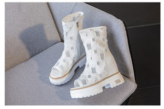 posée sur un fauteil gris , une paire de bottes blanches d'été, basses, en dentelle avec des motifs carrés, et ouvertes sur les orteils