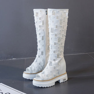 posée sur le sol en carrelage gris, une paire de bottes blanches en dentelle avec motifs de carré